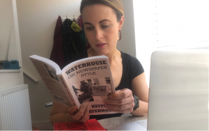 News Associates Manchester part-time trainee Gemma Corby wearing a black t-shirt with her dark blonde hair tied back and hoop earrings sitting down reading Waterhouse on Newspaper Style by Keith Waterhouse in front of a laptop.