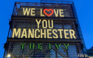 Photo of We Love You Manchester sign outside the Ivy, lit up with a loveheart replace the o in love