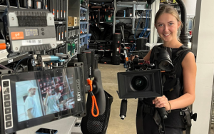 A photo of Izi on her work placement with Beat Media Group. She is holding a large camera and is smiling for a photo.