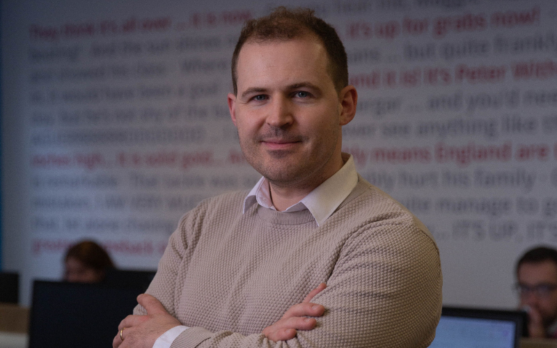 Photo of News Associates media law tutor Charlie Moloney posed in the newsroom with his arms crossed.
